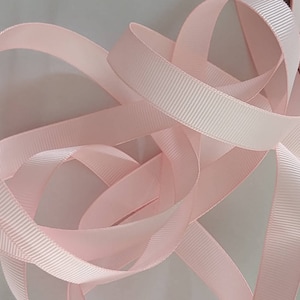 May include: A close-up of a pink satin ribbon with a ribbed texture. The ribbon is folded and twisted, creating a soft and delicate look.
