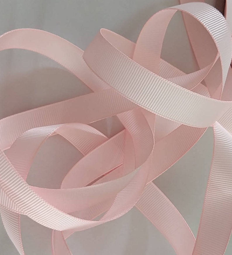 May include: A close-up of a pink satin ribbon with a ribbed texture. The ribbon is folded and twisted, creating a soft and delicate look.