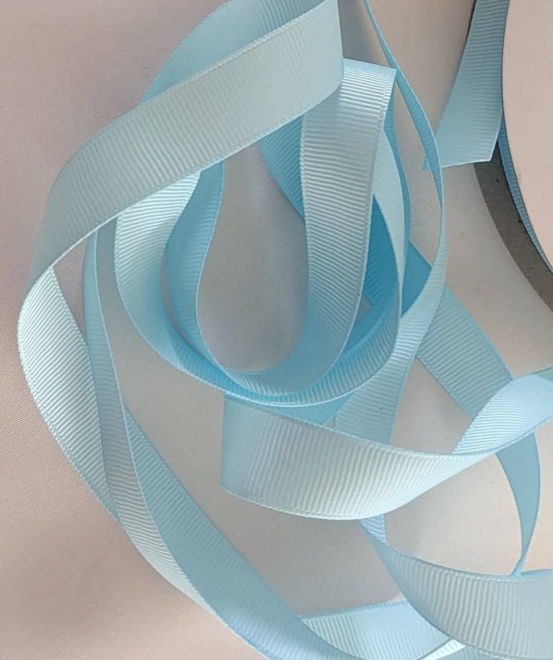 May include: A close-up of a light blue satin ribbon. The ribbon is folded and twisted, showing its texture and sheen.