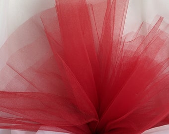 May include: Red tulle fabric, soft and sheer, with a delicate texture. The fabric is gathered and folded, creating a fan-like shape.