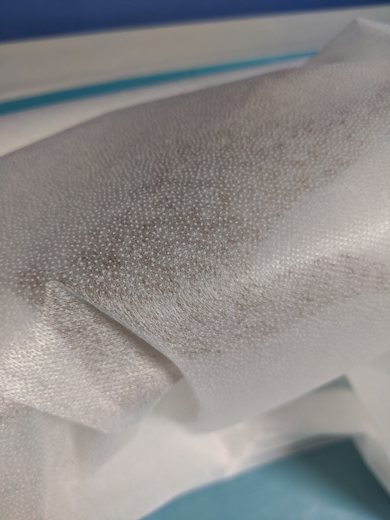 May include: Close-up of white non-woven fabric with a textured surface. The fabric is folded and has a slight sheen.