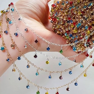 Puede incluir: Primer plano de varias hebras de delicadas cadenas de joyería. Cada cadena está adornada con gemas colgantes de colores en varios tonos. Las cadenas son doradas y plateadas, y las gemas son en tonos de azul, verde, rojo y amarillo.