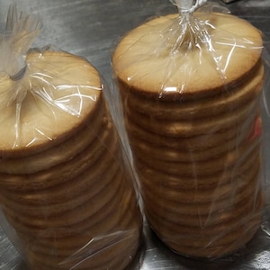 May include: Two clear plastic bags filled with stacks of round, light brown cookies.