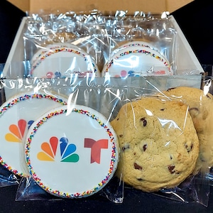May include: A box of assorted cookies, including chocolate chip cookies and decorated sugar cookies with the NBC logo and the letter "T".