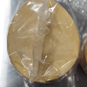 May include: A single, round, light brown tortilla wrapped in clear plastic.