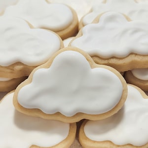 May include: A close-up of several sugar cookies decorated with white frosting in the shape of clouds.