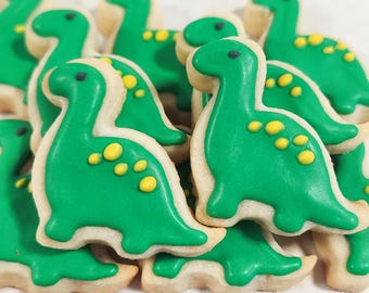 May include: A close-up of green sugar cookies decorated with yellow icing dots, shaped like dinosaurs.