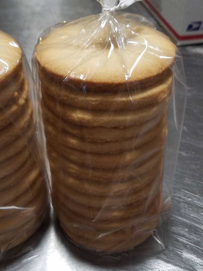 May include: Two bags of round, light brown cookies stacked high. The cookies are in clear plastic bags.