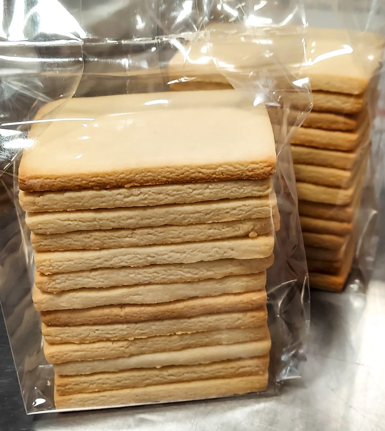 May include: A stack of plain, rectangular cookies in a clear plastic bag. The cookies are light brown and have a slightly rough texture.