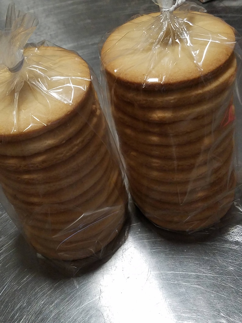 May include: Two clear plastic bags filled with stacks of round, light brown cookies.