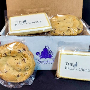 May include: A white box filled with cookies. The cookies are individually wrapped in clear plastic bags. Two of the cookies are decorated with the logo "The Jolley Group". The box is labeled "Storybook Bakery".