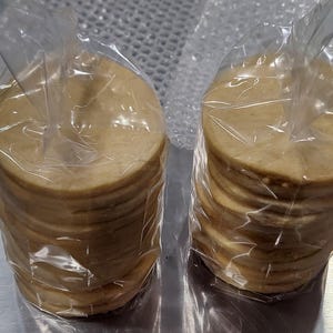 May include: Two stacks of round, beige tortillas wrapped in clear plastic bags. The tortillas are stacked on top of each other and are ready to be used for making tacos, burritos, or other Mexican dishes.