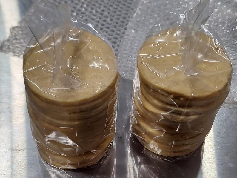 May include: Two stacks of round, beige tortillas wrapped in clear plastic bags. The tortillas are stacked on top of each other and are ready to be used for making tacos, burritos, or other Mexican dishes.