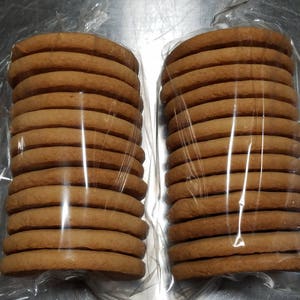 May include: Two packages of round, brown cookies stacked on top of each other. The cookies are wrapped in clear plastic.