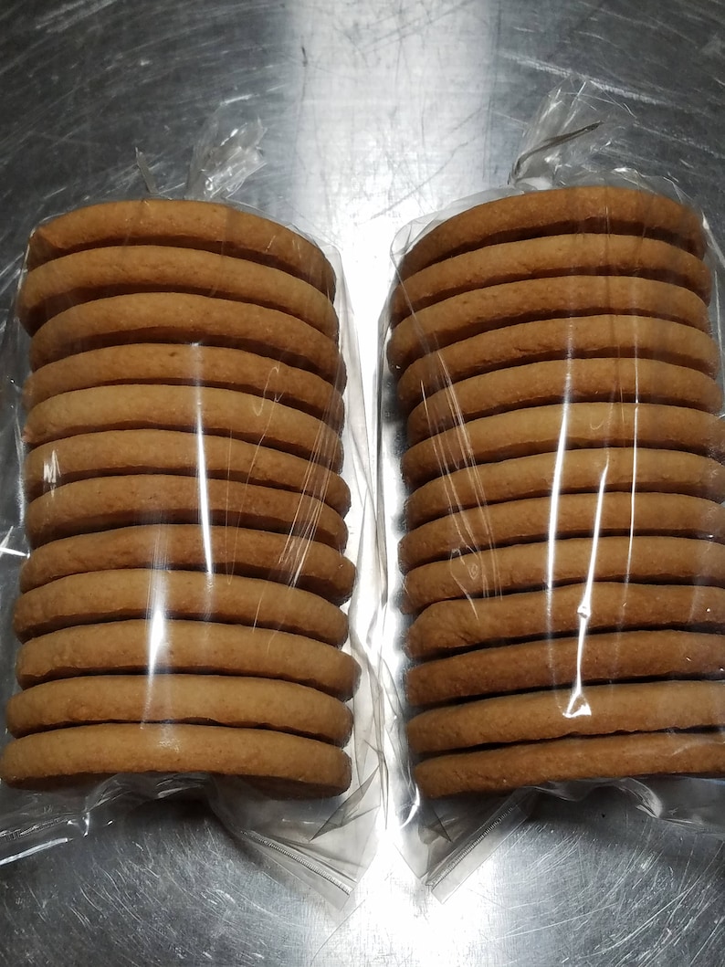 May include: Two packages of round, brown cookies stacked on top of each other. The cookies are wrapped in clear plastic.