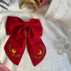 K&ouml;nnte beinhalten: Ein roter Fliege mit gestickten gelben Halbmonden und rosa Blumen.