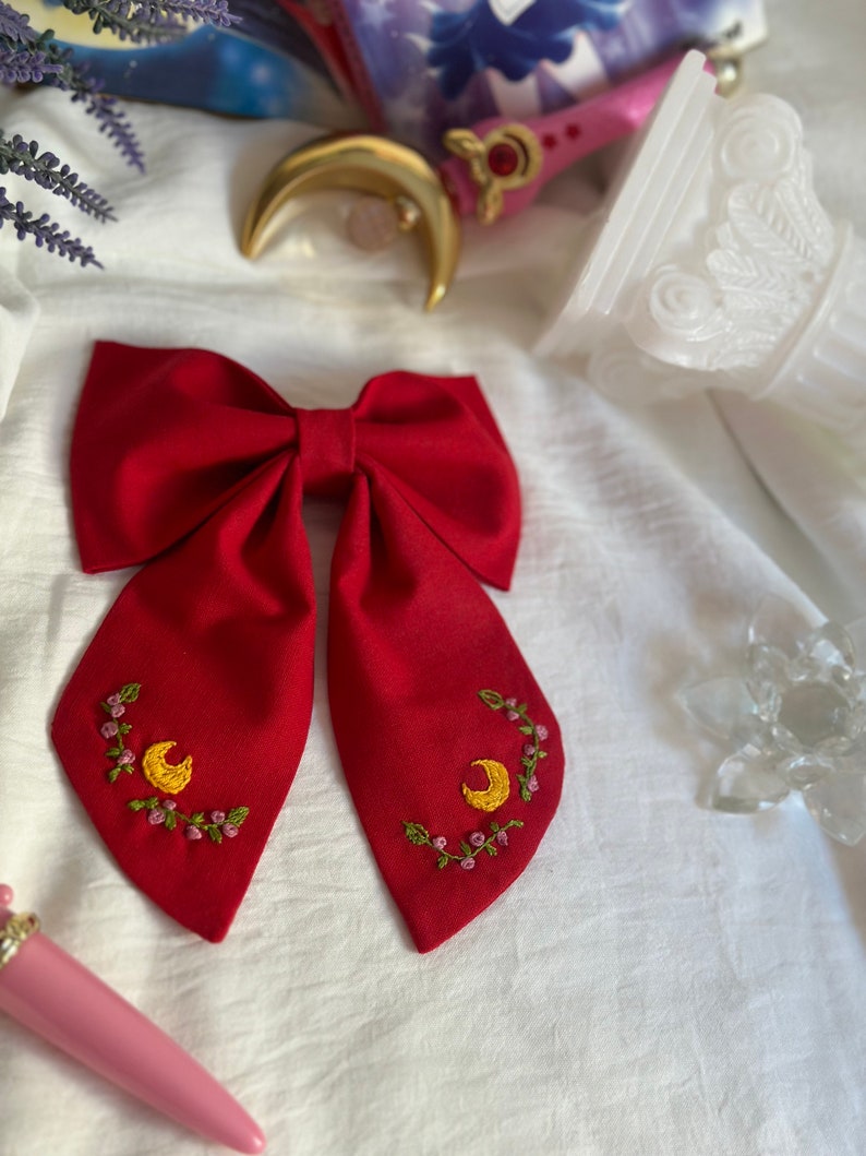 K&ouml;nnte beinhalten: Ein roter Fliege mit gestickten gelben Halbmonden und rosa Blumen.