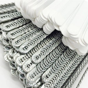 Puede incluir: Primer plano de una pila de perchas de metal plateado con una pila de perchas de plástico blanco en la parte superior.