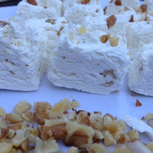 May include: A white plate with several squares of white nougat topped with chopped almonds. The nougat is arranged in a row, and there are some chopped almonds scattered around the nougat.