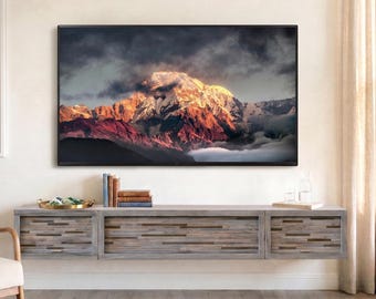 May include: A wall-mounted wooden media console with a textured, multi-tonal finish, positioned below a large television displaying a mountain landscape. To the left, a cream-colored armchair features a navy and white striped throw blanket.