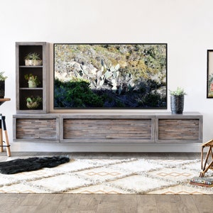 May include: A modern living room setup featuring a large wooden entertainment center with a mounted TV. The room includes a patterned rug, a wicker chair, and decorative plants in pots, creating a stylish and inviting space.