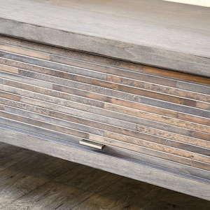 May include: A wooden cabinet with a sliding door. The door is made of horizontal wooden slats in shades of brown, gray, and tan, framed by metal. The cabinet has a matching wooden top and a metal handle.