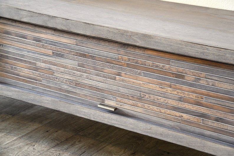 May include: A wooden cabinet with a sliding door. The door is made of horizontal wooden slats in shades of brown, gray, and tan, framed by metal. The cabinet has a matching wooden top and a metal handle.