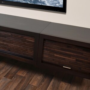 May include: A dark brown, wall-mounted entertainment unit with two sections. The cabinet doors feature a textured, horizontal wood slat design. Silver handles are visible. The top surface is a smooth, dark grey.