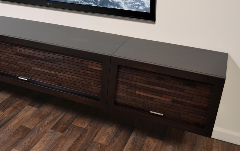 May include: A dark brown, wall-mounted entertainment unit with two sections. The cabinet doors feature a textured, horizontal wood slat design. Silver handles are visible. The top surface is a smooth, dark grey.