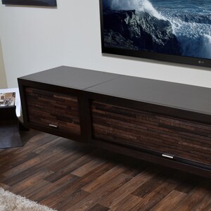 May include: A contemporary, dark brown TV unit with two sliding doors, each with a textured wooden panel design. The unit is wall-mounted, with a large flat-screen TV above. A magazine rack is visible to the left.