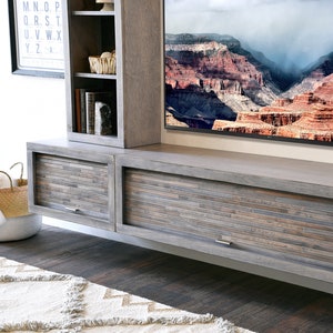 May include: A gray wooden entertainment center with a built-in TV and storage cabinets. The cabinet doors have a mosaic-like design. A woven basket and a rug are in the foreground. The TV displays a scenic landscape.