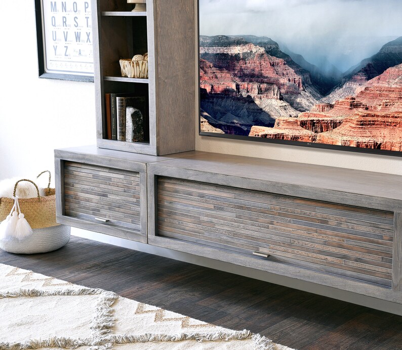 May include: A gray wooden entertainment center with a built-in TV and storage cabinets. The cabinet doors have a mosaic-like design. A woven basket and a rug are in the foreground. The TV displays a scenic landscape.