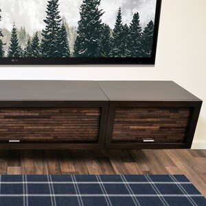 May include: A dark brown floating media unit with two cabinets. The cabinet doors feature a textured, horizontal wood grain design. A blue plaid rug is on the floor. A large TV displays a forest scene.