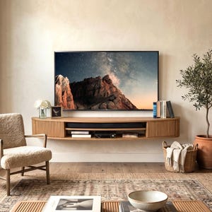 May include: A modern living room with a large flat-screen TV mounted above a wooden media console. A cozy armchair, a potted olive tree, and a woven basket add warmth. A patterned rug and a coffee table complete the inviting space.
