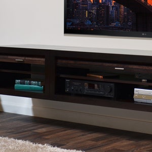 May include: A dark brown, wall-mounted entertainment unit with open shelving and drawers. The unit has a built-in shelf with a stereo receiver and a DVD player. A large flat-screen TV is mounted above the unit.