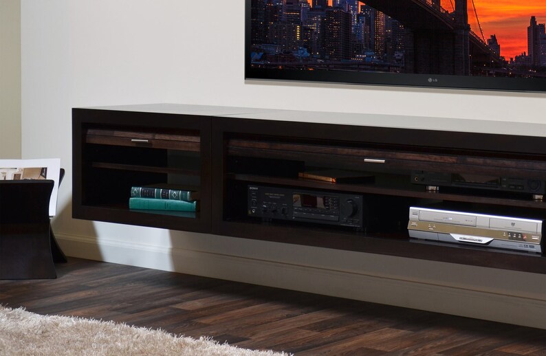 May include: A dark brown, wall-mounted entertainment unit with open shelving and drawers. The unit has a built-in shelf with a stereo receiver and a DVD player. A large flat-screen TV is mounted above the unit.