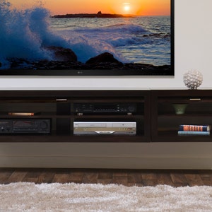 May include: A dark brown, wall-mounted entertainment unit with several compartments. It has a TV above and a DVD player, receiver, and other media components inside. A decorative sphere sits on top.