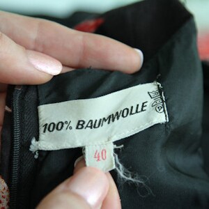 May include: Close-up of a black fabric label with white text that reads "100% Baumwolle" and "40". The label is attached to a black garment.