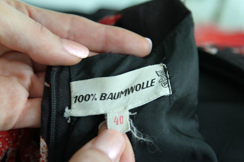 May include: Close-up of a black fabric label with white text that reads "100% Baumwolle" and "40". The label is attached to a black garment.