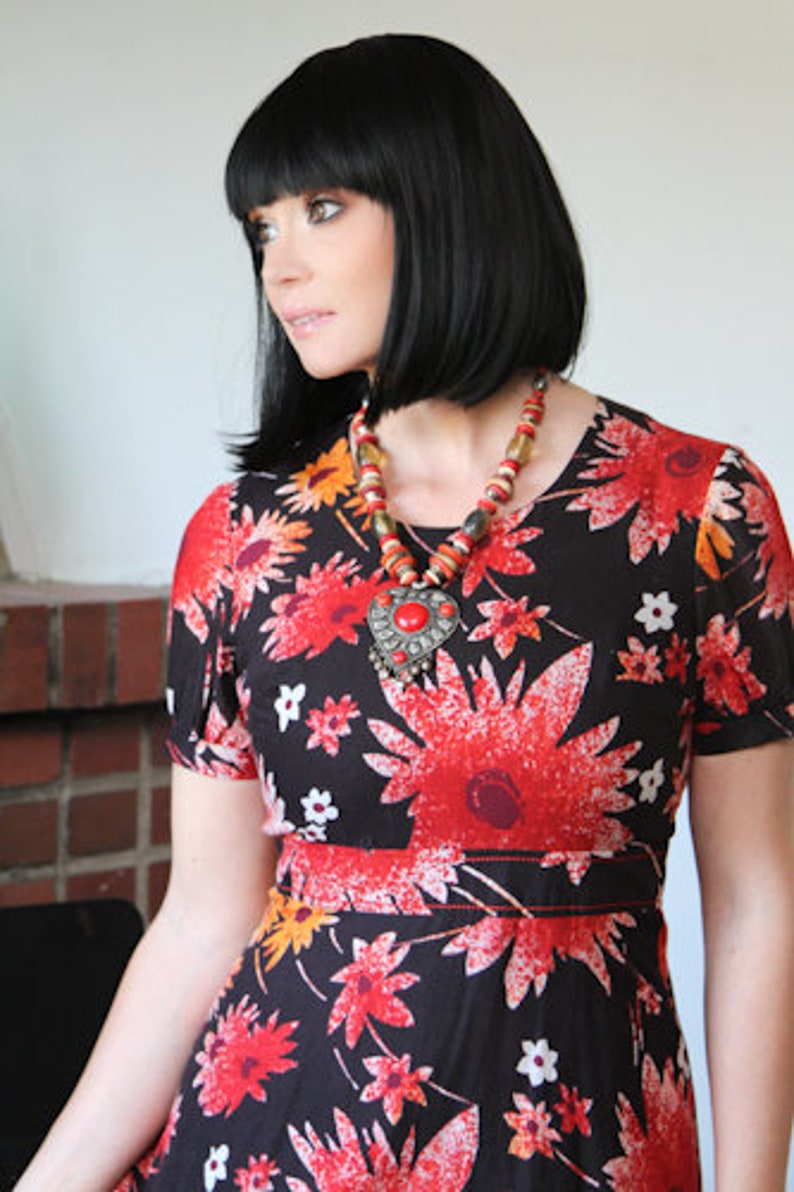 May include: A woman with black hair wearing a black and red floral dress with a large red pendant necklace.