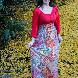 K&ouml;nnte beinhalten: Eine Frau tr&auml;gt ein rot-blaues Maxikleid mit Paisley-Muster. Das Kleid hat ein tailliertes Oberteil und einen flie&szlig;enden Rock. Sie steht auf einem Feld mit gelben Bl&auml;ttern.