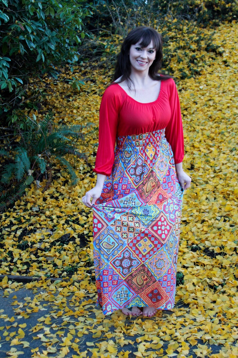 K&ouml;nnte beinhalten: Eine Frau tr&auml;gt ein rot-blaues Maxikleid mit Paisley-Muster. Das Kleid hat ein tailliertes Oberteil und einen flie&szlig;enden Rock. Sie steht auf einem Feld mit gelben Bl&auml;ttern.