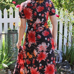 May include: A long black maxi dress with a floral print featuring red, orange, and white flowers. The dress has a V-neckline and short sleeves.