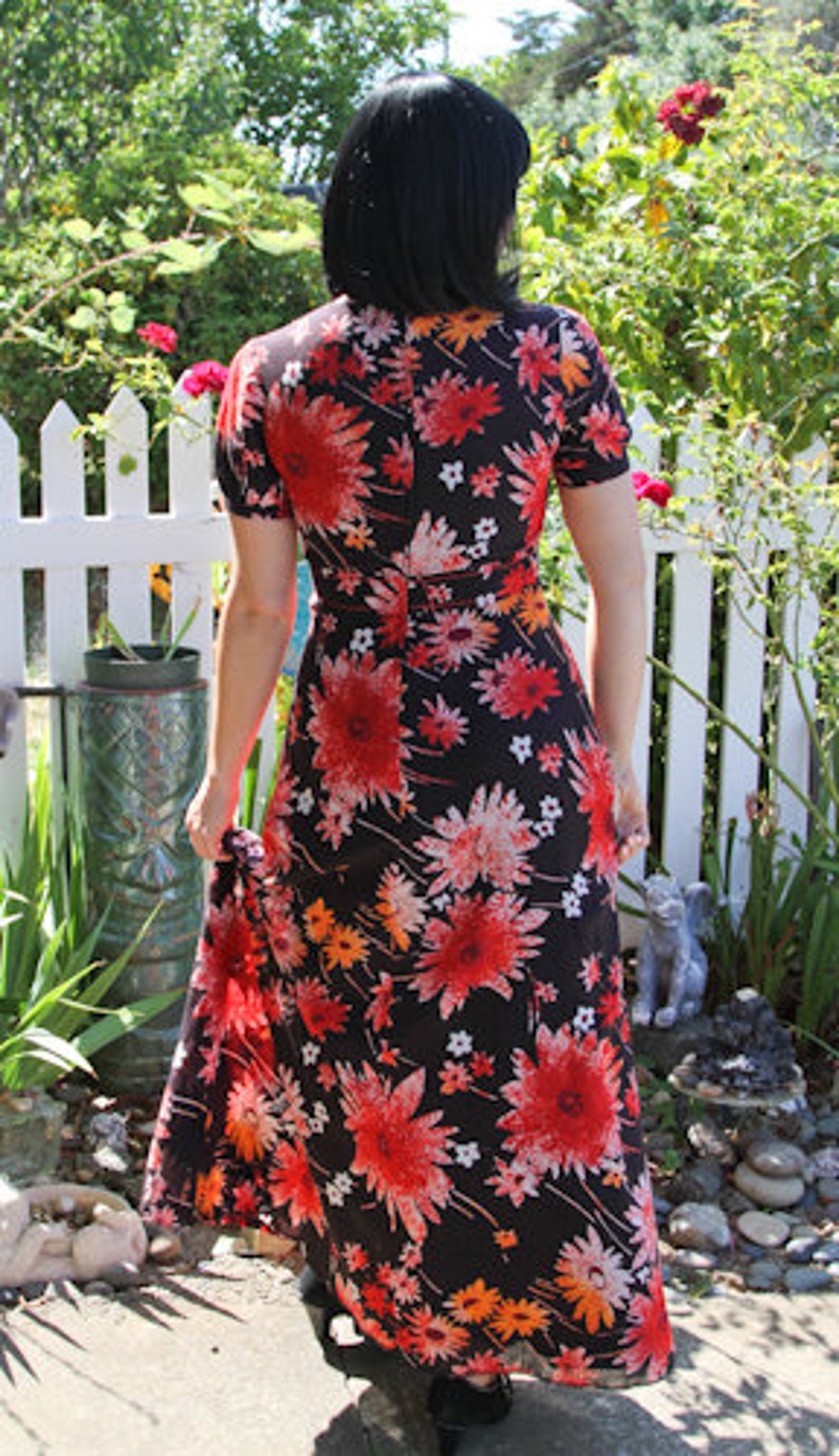 May include: A long black maxi dress with a floral print featuring red, orange, and white flowers. The dress has a V-neckline and short sleeves.