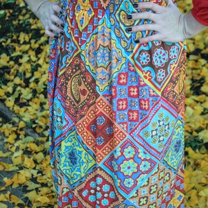 K&ouml;nnte beinhalten: Ein langer, rot-blauer, gemusterter Rock mit einem elastischen Bund. Der Rock hat ein Patchwork-Design mit verschiedenen geometrischen Formen und Paisley-Mustern.