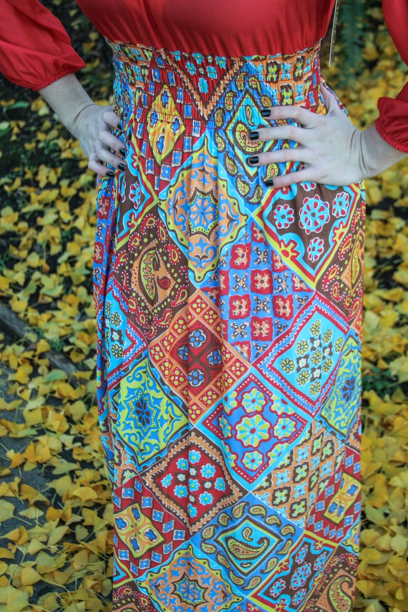 K&ouml;nnte beinhalten: Ein langer, rot-blauer, gemusterter Rock mit einem elastischen Bund. Der Rock hat ein Patchwork-Design mit verschiedenen geometrischen Formen und Paisley-Mustern.