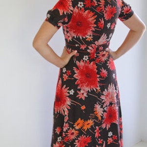 May include: A long, flowing maxi dress with a floral print. The dress is black with red, orange, and white flowers. The dress has a V-neckline and short sleeves.