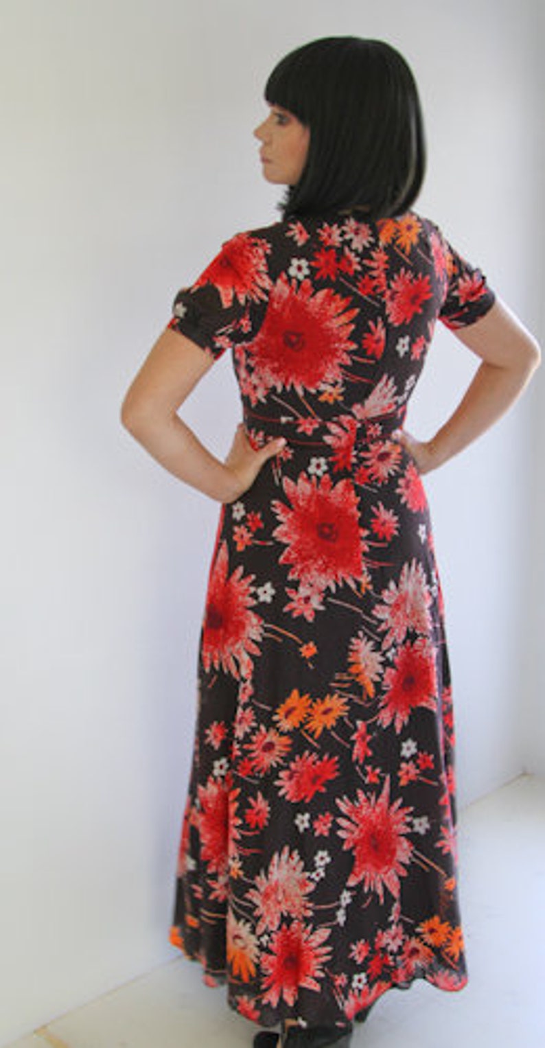 May include: A long, flowing maxi dress with a floral print. The dress is black with red, orange, and white flowers. The dress has a V-neckline and short sleeves.