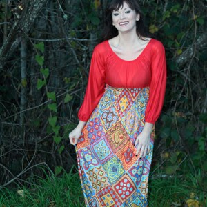 K&ouml;nnte beinhalten: Eine Frau tr&auml;gt ein rotes Langarm-Oberteil mit einem bunten gemusterten Rock. Der Rock hat ein Patchwork-Design mit geometrischen Formen und Paisley-Mustern.