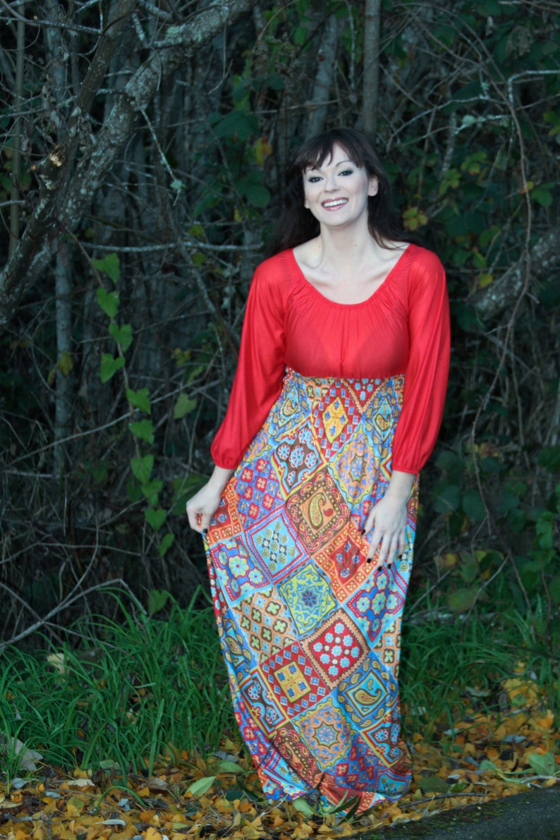 K&ouml;nnte beinhalten: Eine Frau tr&auml;gt ein rotes Langarm-Oberteil mit einem bunten gemusterten Rock. Der Rock hat ein Patchwork-Design mit geometrischen Formen und Paisley-Mustern.